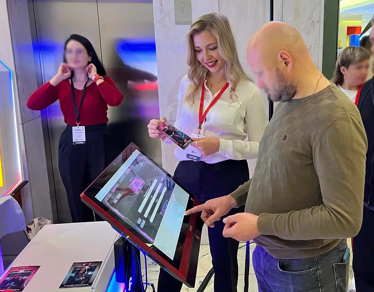 Ассистент вручает напечатанное фото гостю у сенсорной станции отправки