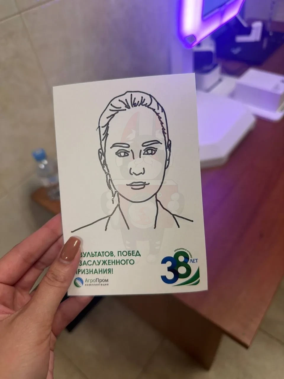 Открытка в руке: портрет, нарисованный роботом маркером, поздравление и логотип «38 лет» агрохолдинга