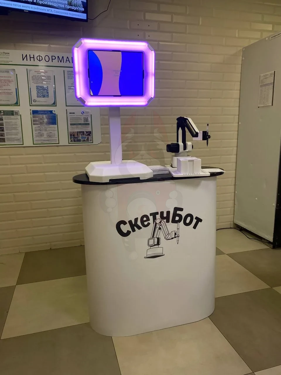 Скетчбот на фирменной тумбе: планшет в подсвеченной рамке и робот-манипулятор с маркером у информационного стенда компании