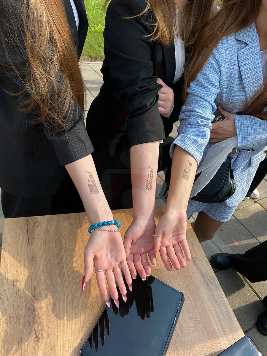 Три студентки показывают одинаковые парные тату от Prinker на запястьях