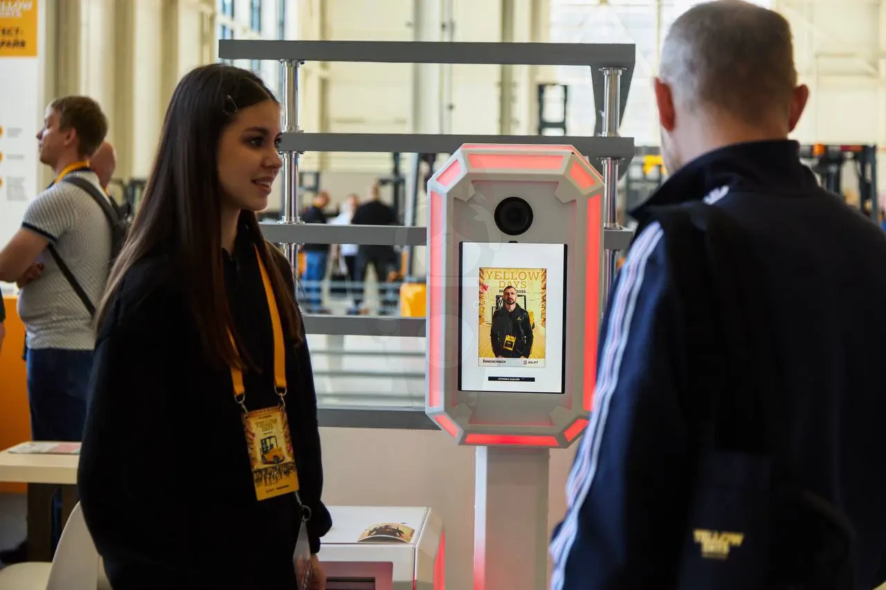 Оператор фотобудки MixUp показывает результат нейросети посетителю выставки складской техники